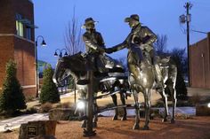 two statues of men on horses in front of a brick building at night with street lights