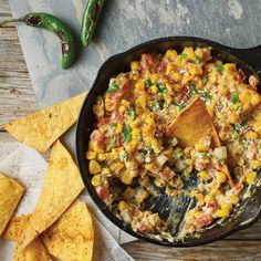 a skillet filled with mexican food next to tortilla chips and jalapenos