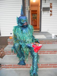 a man in a monster costume sitting on the front steps of a house holding a candy bar