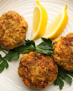 three crab cakes on a white plate with lemon wedges