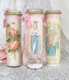 three decorated candles sitting on top of a white lace covered table next to a pink rose