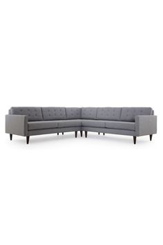 a gray sectional couch with wooden legs and buttons on the back, in front of a white background