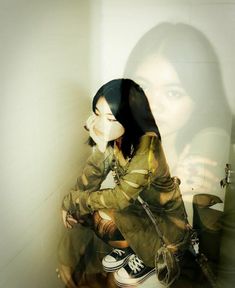 a woman sitting on top of a toilet next to a wall with her hand in her mouth