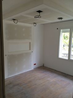 an empty room with white walls and wood flooring in the foreground is a window