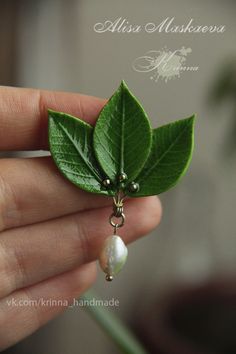 a person holding a green leaf and pearl droplet broochle in their hand