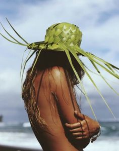 a woman wearing a straw hat on top of her head at the ocean's edge