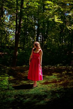 a woman in a red dress is standing in the woods with her hand on her hip