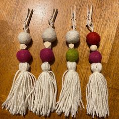 four tassels are lined up on a wooden table, each with different colored balls and tassels