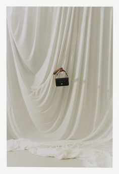 a hand holding a black purse in front of a white curtain with the light coming through it