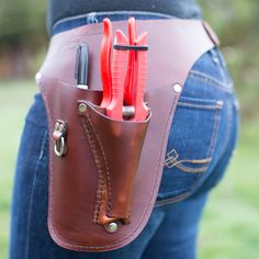 a woman holding a leather tool belt with tools in it's pocket and two knives sticking out of the back