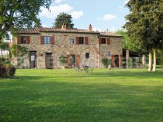 an old stone house in the middle of a green field with tables and chairs around it