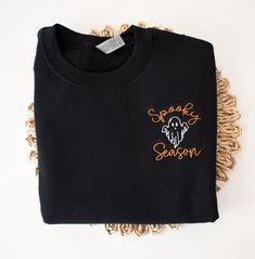 Our new Spooky Season Halloween Sweatshirt is the perfect addition to your Fall and Halloween wardrobe. This embroidered sweatshirt is professionally embroidered and will definitely get you excited for Fall and Halloween!  Professionally embroidered with left chest placement.  Sweatshirt is a 8 oz. 50/50 cotton/polyester blend fleece Spooky season will be embroidered with our premium orange thread. The ghost will be embroidered with black thread on the following colors - White, Sand, Light Blue, Black Cotton Halloween Sweater, Black Embroidered T-shirt For Fall, Black Cotton Sweater With Letter Embroidery, Custom Embroidered Long Sleeve Top For Halloween, Black Fall Sweater With Embroidered Text, Black Sweater With Embroidered Text For Fall, Black Embroidered Text Sweater For Fall, Black Embroidered Tops For Halloween, Halloween Embroidered Long Sleeve Tops