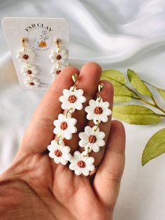 a pair of white and brown flower earrings in the palm of someone's hand