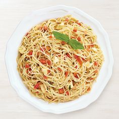 a white bowl filled with pasta and topped with fresh basil leaves on top of a wooden table