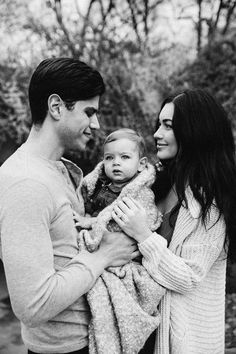 a man holding a baby in his arms while standing next to a woman with her arm around him