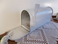 a white mailbox sitting on top of a wooden table next to a doily