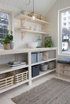 a white room with shelves and baskets on the floor next to a window filled with potted plants