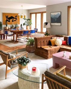 a living room filled with lots of furniture next to large windows and potted plants