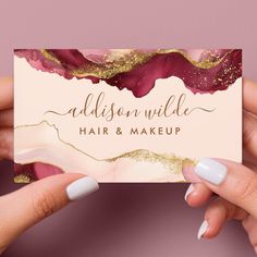 two hands holding up a business card with gold and burgundy paint on it, which reads madison wilde hair & makeup