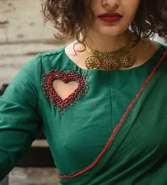 a woman wearing a green top with a heart on the chest and red beads around her neck