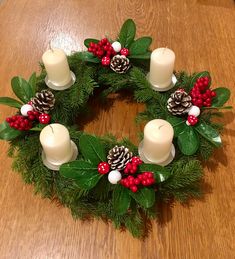 a christmas wreath with candles and holly leaves on a wooden table next to a candle