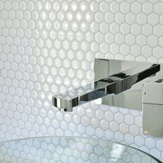 a chrome faucet mounted to the side of a white tiled wall next to a glass table