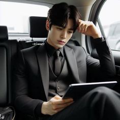 a man in a suit sitting in the back seat of a car looking at his tablet