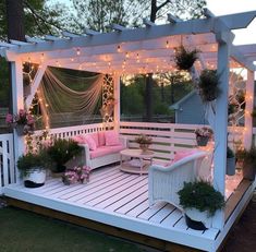 an outdoor deck with white furniture and string lights on the ceiling, surrounded by potted plants