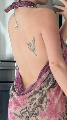 a woman with a bird tattoo on her back is standing in front of a refrigerator