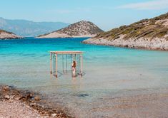 a person standing in the water with a small structure on it's head and mountains in the background