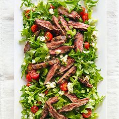 steak salad with tomatoes, lettuce and feta cheese on a white platter