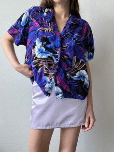 Purple & blue multi-color printed short sleeve collared tee by Jams World with purple buttons down the front. Unlined with a boxy fit. In excellent vintage condition. DETAILSLabel: Jam's WorldMade in USAMaterial: 100% Rayon SIZE & MEASUREMENTSTag Size: Large Best Fits: XS/Small Length: 22" Bust: 44"Waist: 44"Sleeve: 8"Shoulder: 18" Purple Printed Shirt With Short Sleeves, Purple Collared Top With Graphic Print, Purple Floral Print Short Sleeve Tops, Retro Short Sleeve Purple Shirt, Retro Purple Short Sleeve Shirt, Retro Purple Short Sleeve Top, 90s Style Purple Short Sleeve Tops, Purple Short Sleeve 90s Tops, Purple Floral Print Short Sleeve Shirt