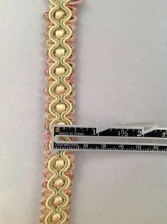 a measuring tape is attached to a piece of fabric with gold and pink braiding