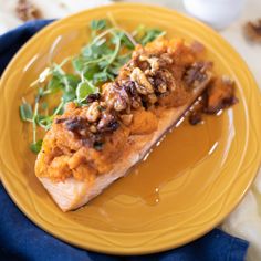 a yellow plate topped with fish covered in nuts and greens on top of a blue cloth