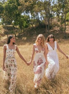 three women walking through tall grass holding hands