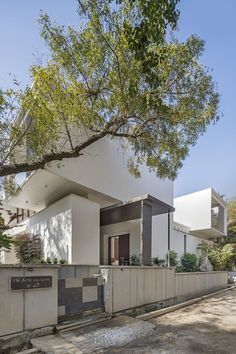 a white house on the side of a road with trees and bushes in front of it