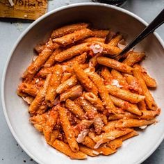 a white bowl filled with pasta and meat on top of a table next to a fork