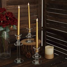 three candles sitting on top of a wooden table next to a vase with flowers in it