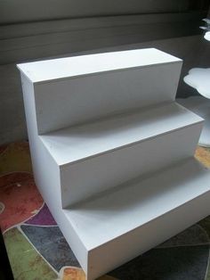 three white shelves stacked on top of each other in front of a table with flowers