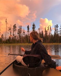 a woman is sitting in a canoe on the water and pointing at something with her hand