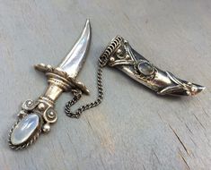 two silver objects on a wooden surface one has a knife and the other is a chain