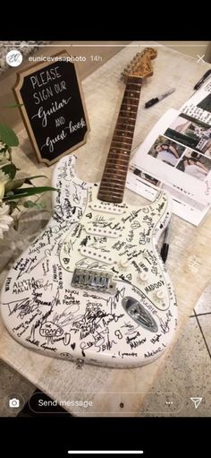 an electric guitar with writing on it sitting on a table next to flowers and pictures