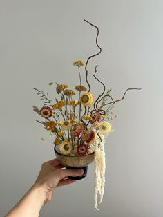 a hand holding a vase with dried flowers in it