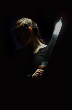 a woman holding a large knife in the dark with light coming through her face and behind her head