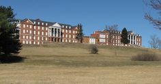 a large building on top of a hill with trees in the foreground and grass below