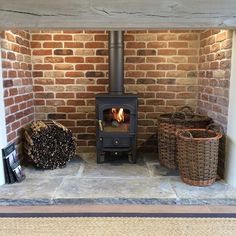 a wood burning stove sitting inside of a brick fireplace next to two wicker baskets