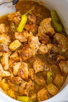 a white crock pot filled with chicken and green peppers next to a wooden spoon