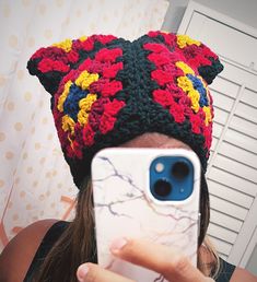 a woman taking a selfie with her cell phone wearing a crocheted hat