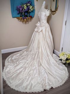 a white wedding dress on display in front of a blue wall and mirror with flowers