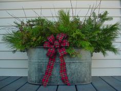 a metal bucket filled with plants on top of a wooden table next to a house